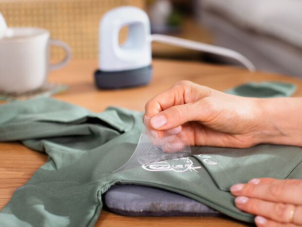 Support thermocollant en cours de retrait d'un motif sur un t-shirt vert.